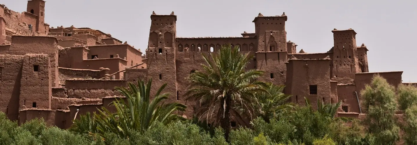 La antigua Kasbah Ait Ben Haddou con sus características estructuras de arcilla roja, enmarcadas por exuberantes palmeras verdes, captadas durante una experiencia turística de 3 días.