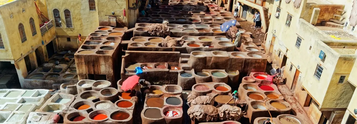 Obreros trabajando en las históricas curtidurías de Fez, rodeados de coloridas fosas de tintes, como parte de la experiencia cultural de una excursión de 3 días desde Fez al desierto.